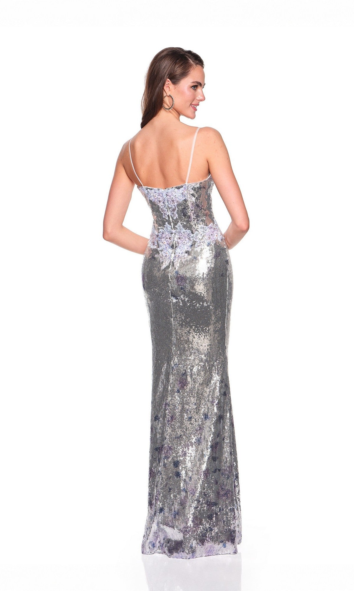 A woman models the Dave and Johnny 12703 long prom dress, featuring silver sequins and thin straps, as she stands facing away to highlight its elegant back against a white background.